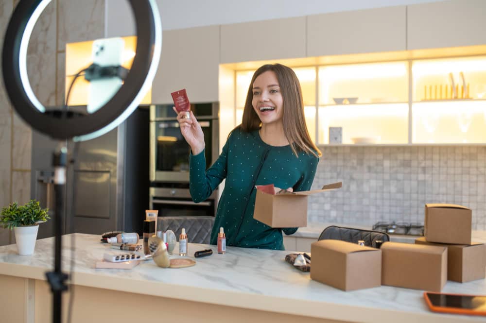 A smiling woman is recording a video showcasing product content for her online audience in her home setting.